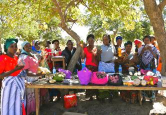 Group of people displaying fresh produce and food products at an outdoor table.