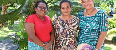 Three women standing in front of palm trees, smiling at the camera.