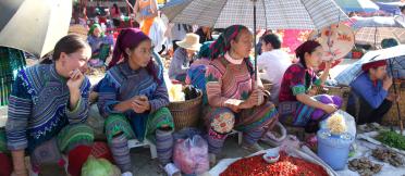 A group of people sitting on the ground and holding umbrellas, displaying produce, including chillis for sale