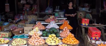 Market vendor standing next to displays of fruit and vegetables