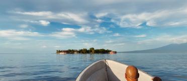 A person sitting in a boat on calm waters with an island in the distance.