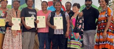 Group of participants standing on a stage holding certificates, with ACIAR and Australian Aid banners behind them.