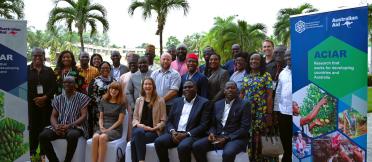 Group of workshop participants seated and standing outdoors beside ACIAR banners.