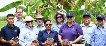 A group of project partners standing in a banana plantation, holding baskets of harvested rice.