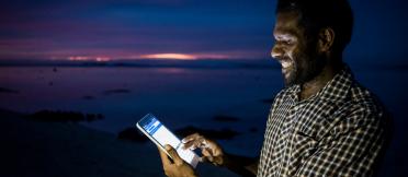 Male using a tablet with the screen glowing against the dark ocean backdrop.