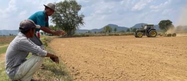 Two farmers observe a tractor levelling a field.