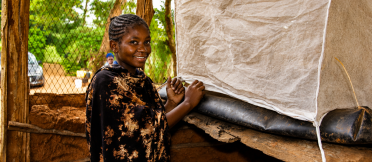Person standing beside an insect-rearing enclosure covered with mesh fabric.