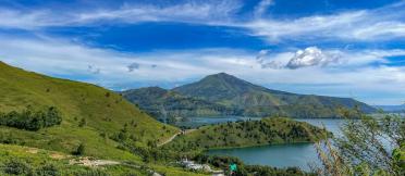 Green hills and a lake surrounded by mountains under a bright blue sky.