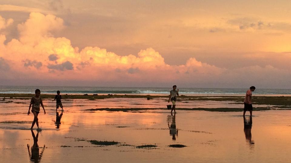 Children walking along a beach at sunset, holding buckets