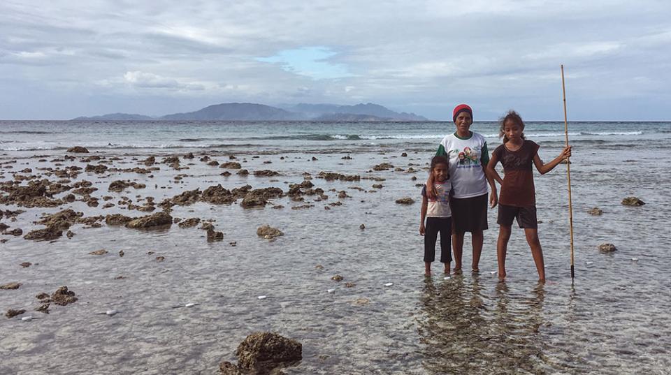 Three people standing in the shallows of the ocean with a fishing spear