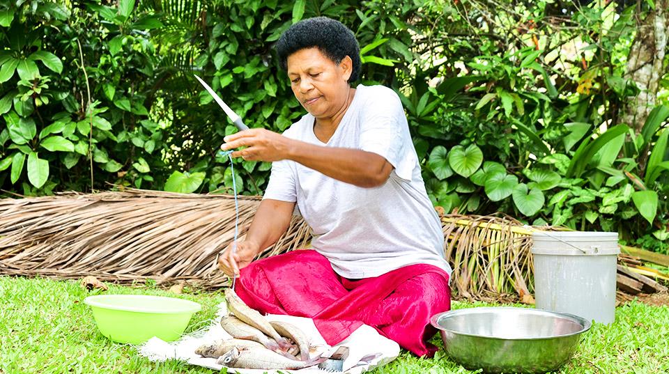 a woman holding a knife, sitting in front of some fish