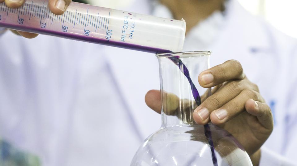 person in a lab coat, pouring liquid