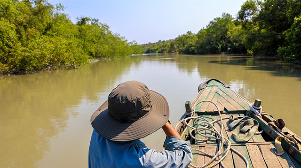 a man travels by boat on a wide river canal in Bangladesh. trees on both river banks.