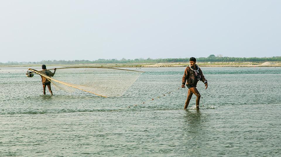 two men in shallow waters using a fishing net