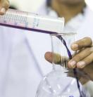 person in a lab coat, pouring liquid