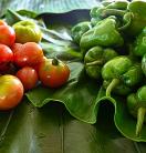 Fresh tomatoes and capsicums neatly arranged over banana leaves