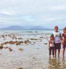 A woman and two young girls in ankle-deep, clear, sea water.
