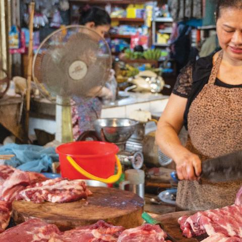 woman at a market cutting up raw meat
