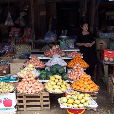 Market vendor standing next to displays of fruit and vegetables