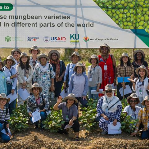 A large group of people, mostly wearing hats outdoors in front of a large sign