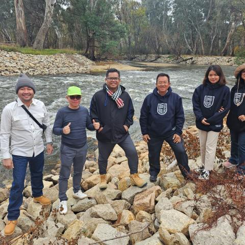 A group of six people standing on a rock river bank with the river in the background