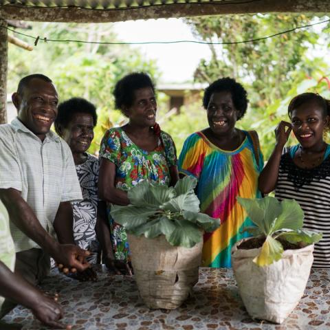 A group of people staning around a table containing two plants