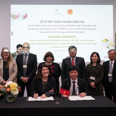 A group of people signing documents at a table and smiling at the camera
