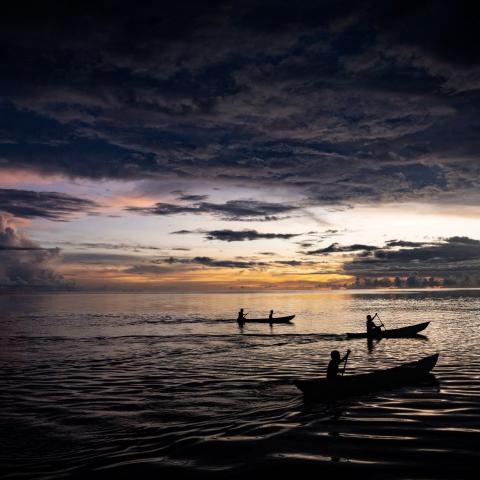 A group of people in canoes on the water at sunset