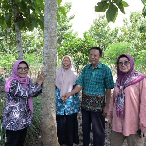 Participants gathered beside a tree during a field visit in a forest setting.