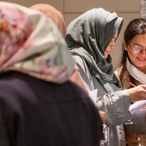 Women standing together indoors, reviewing documents and discussing notes during a collaborative workshop.