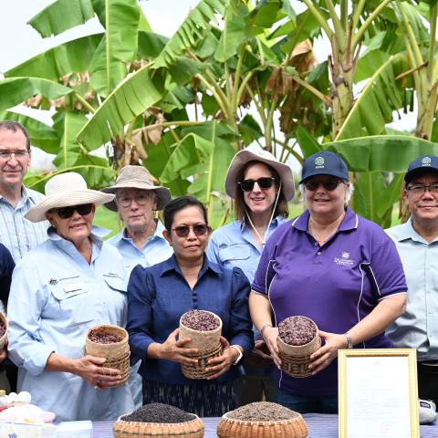 A group of project partners standing in a banana plantation, holding baskets of harvested rice.