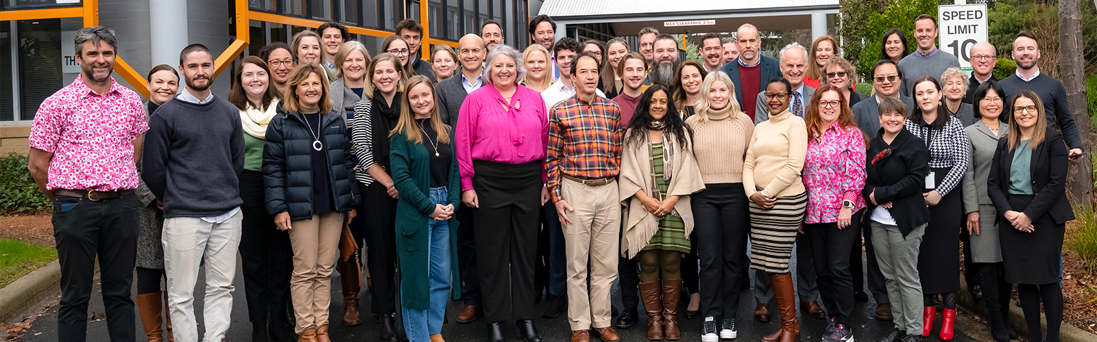 A group photo of around 30 men and women standing in front of an office building.