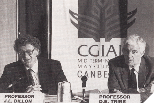 Black-and-white photo of two men sitting behind a table with microphones in front of them. They’re both wearing suits and ties and one man has glasses. Behind them is a sign that says CGIAR.