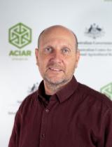 Bio headshot image of Dr Nick Harris standing in front of ACIAR banner