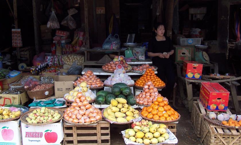 Market vendor standing next to displays of fruit and vegetables