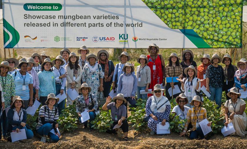 A large group of people, mostly wearing hats outdoors in front of a large sign