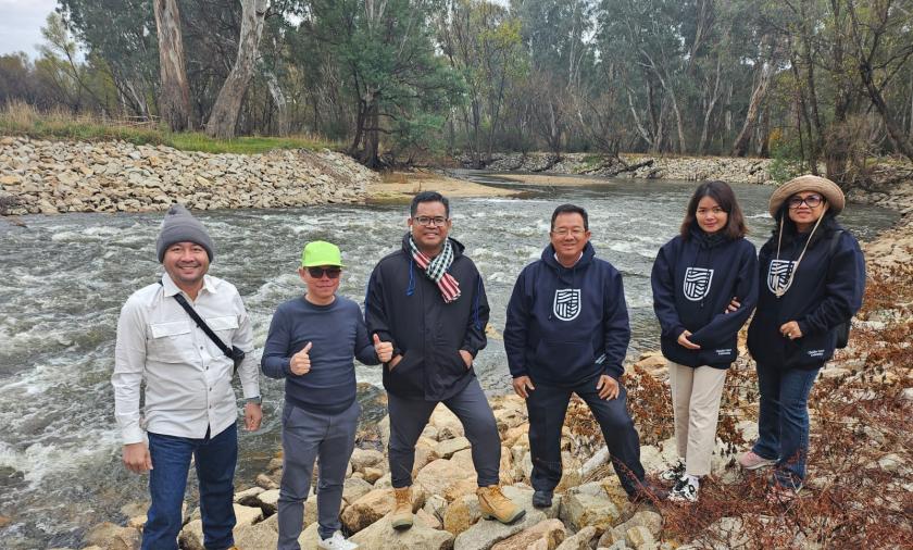 A group of six people standing on a rock river bank with the river in the background
