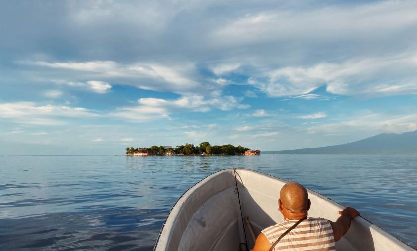 A person sitting in a boat on calm waters with an island in the distance.